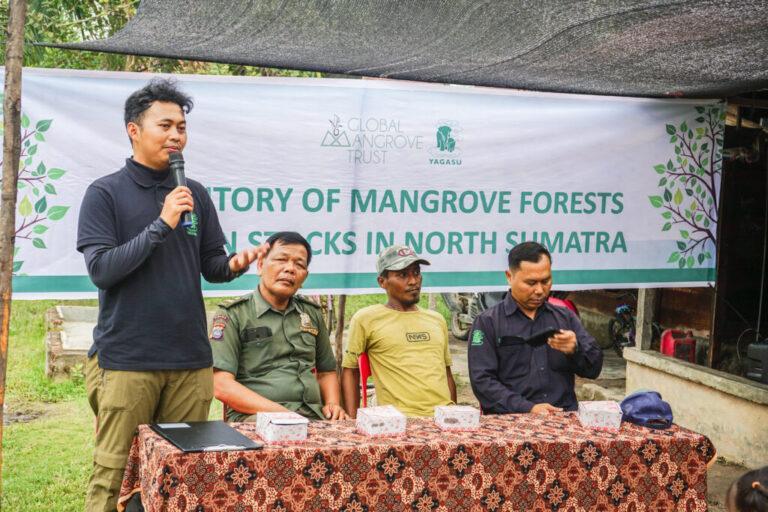 A banner reading 'history of mangrove forests' hangs above a group of people seated at a table. GMT and YAGASU define project boundaries